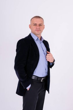 Mavi gömlekli, siyah pantolonlu ve beyaz arka planda mavi ceketli bir adam.