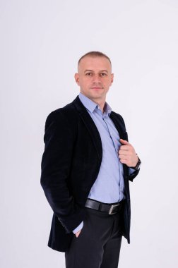 Mavi gömlekli, siyah pantolonlu ve beyaz arka planda mavi ceketli bir adam.