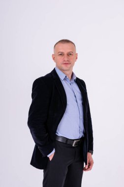 Mavi gömlekli, siyah pantolonlu ve beyaz arka planda mavi ceketli bir adam.