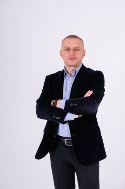 Mavi gömlekli, siyah pantolonlu ve beyaz arka planda mavi ceketli bir adam.