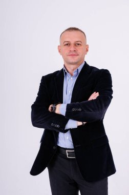 Mavi gömlekli, siyah pantolonlu ve beyaz arka planda mavi ceketli bir adam.