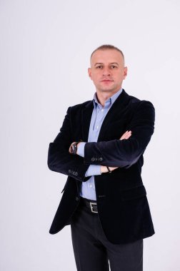 Mavi gömlekli, siyah pantolonlu ve beyaz arka planda mavi ceketli bir adam.