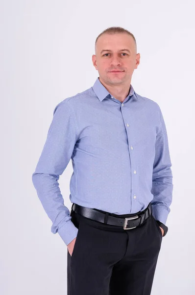 Mavi gömlekli ve siyah pantolonlu bir adam beyaz arka planda duruyor.