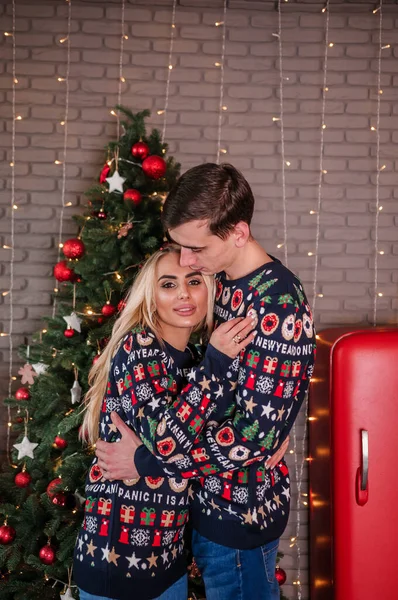 一个男人穿着毛衣和牛仔裤 抱着一个女孩 在圣诞树和红色礼物的背景上亲吻 — 图库照片