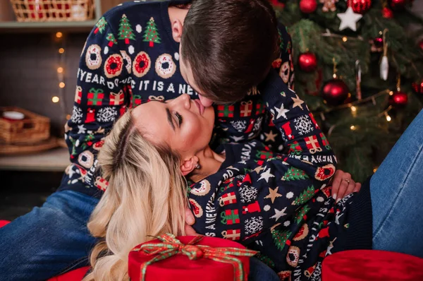 A guy with a girl in a sweater and jeans are hugging on the background of a Christmas tree and red gifts — Stock Photo, Image