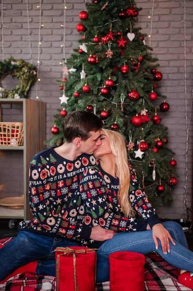 Um cara com uma garota em uma camisola e jeans estão abraçando no fundo de uma árvore de Natal e presentes vermelhos — Fotografia de Stock