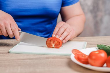 A man cuts a red tomato on a board. Cucumbers and tomatoes in a white plate