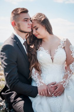 Yeni evliler kayaların ve güzel manzaranın arka planında sarılırlar.