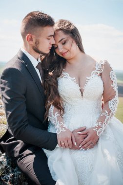 Yeni evliler kayaların ve güzel manzaranın arka planında sarılırlar.