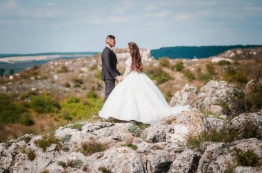 Yeni evliler güzel bir manzaranın arka planında sarılırlar.