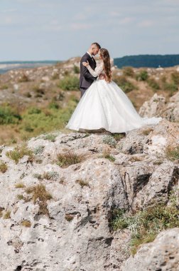 Yeni evliler güzel bir manzaranın arka planında sarılırlar.