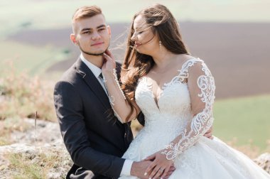 Yeni evliler güzel bir manzaranın arka planında sarılırlar.