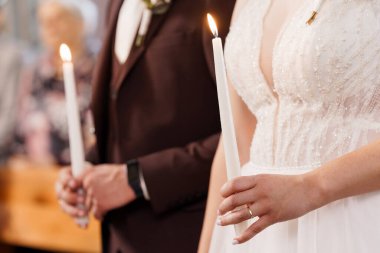 Romantik düğün sahnesi, gelin ve damadın birlik mum seremonisine katılması. Geleneksel beyaz elbiseler, resmi takım elbiseler ve yumuşak kilise ışıklandırması. Aşkı ve bağlılığı simgeler.