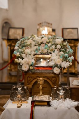 Ortodoks düğün töreninin güzel bir tasvirinde sunağı süsleyen, sevgi ve inancı sembolize eden, altın bir kadehle birlikte beyaz bir çiçek aranjmanı yer alıyor.