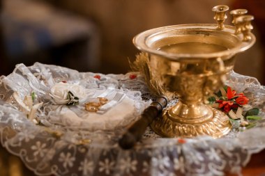 Close-up shot of a richly ornamented golden baptismal font with a lace cloth, white candles, and rose decorations in a solemn church ceremony