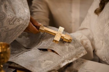 Süslü bej giysiler içinde bir Ortodoks rahibinin resmi dini ayin sırasında elinde altın bir haç tutarken, dini inancı ve Hıristiyan ruhaniliğini gösteren yakın plan bir görüntüsü.