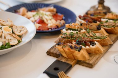 Close-up shot of an artfully arranged bruschetta platter with various toppings on a white table, presenting rustic wooden boards and blue plates, highlighting Italian cuisine appetizers
