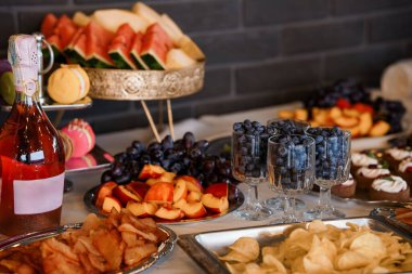 Şampanyalı, pastalı ve çeşitli atıştırmalık güzel bir meyve tabağı koyu renkli bir tezgahta sergileniyor. Kutlama için zarif bir yemek servisi sunuluyor.