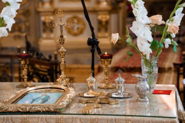 Kadehler, haçlar ve çerçevelenmiş bir simge de dahil olmak üzere karmaşık altın ayin nesneleri geleneksel bir kilise ayini sırasında çiçek aranjmanları ile çevrili beyaz bir sunak süsler.