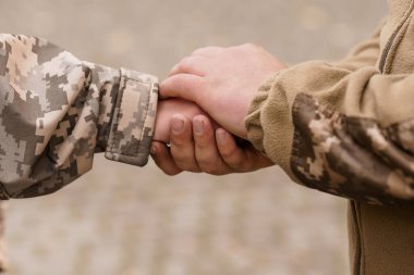 İki asker, askeri bağlamda dostluk, destek ve güven göstergesi olarak el ele tutuşuyor. Görüntü, tozlu bir ortamda birlik hissi ve ortak bir amaç taşır.