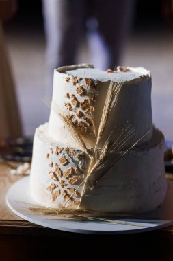 Gri desenli kremalı ve doğal buğday saplı güzel dekore edilmiş iki katlı düğün pastası kırsal kutlamalar, çiftlik evleri düğünleri ve tatlı betimlemeleri için idealdir.