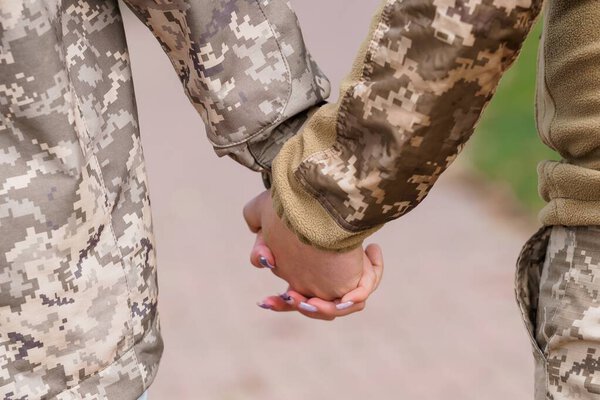 Two U.S. Army soldiers in digital camouflage uniforms tenderly hold hands outdoors, conveying support and connection. a powerful image representing camaraderie, love, and military relationships