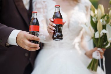 Yeni evli bir çift düğün törenlerinde minyatür Coca-Cola şişeleri tutuyor. Eşsiz bir kutlama anını sembolize ediyor neşeli bir dokunuşla, yaşam tarzı markalaşması için ideal.
