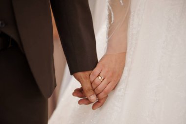 Bir gelin ve damadın el ele tutuşup, altın alyanslarını kahverengi takım elbise ve beyaz dantelli elbiseye karşı sergiledikleri yakın çekim, aşkı simgeliyor.