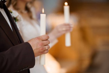 Gelin ve damadın bir kilisenin içindeki birlik mumu seremonisi sırasında çekilmiş yakın çekim, onların birleşmesini sembolize ediyor, yanan mumlara ve paylaşılan ana odaklanıyor.