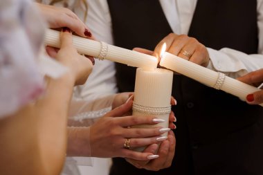 Düğün töreninde özel bir an. Birliktelik mumunu yakan eller. İnci aksanlı beyaz mumlar, altın yüzükler bağlılığı, romantik havayı simgeler.