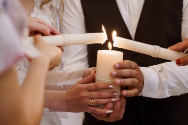 Düğün birlik mum seremonisinin yakın çekimi, beyaz mumların yakılması bağlılığı sembolize ediyor, etkinlik planlaması için romantik ve sıcak bir atmosfer sunuyor.