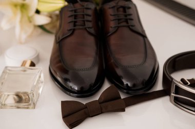 Cilalı kahverengi deri ayakkabılar, uyumlu bir papyon ve kemer ve kolonya şişesinin yanında güzel bir şekilde düzenlenmiş sakin bir hayat. Düğün, moda ya da hediye konseptleri için ideal