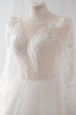 İç çamaşırı ve kollarında ince bir inci kolye ve ince kıvılcımlı bir tül etekle tamamlanmış karmaşık dantelli fildişi bir gelinliğin çarpıcı yakın çekimi.