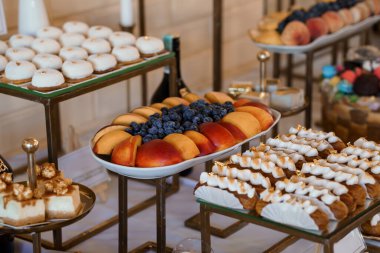 Gösterişli bir tatlı büfesi sunumu çeşitli hamur işleri, taze şeftali ve yabanmersinleri ve bir düğün resepsiyonunda süslenmiş şekerlerle dolu duruyor. Altın aksanlar lüks havayı arttırır.