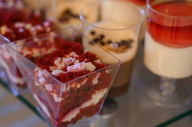 Çikolata ve beyaz çikolata parçalarıyla bezenmiş şeffaf bardaklarla dolu canlı kırmızı kadife pasta katmanları, tatlı sergileri ve kutlamalar için ideal.