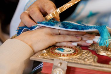 Bir papaz, süslü bir dini metnin üzerine parlak mavi püsküllü bir kumaş yerleştirir. Resmi bir ayin sırasında, karmaşık altın detaylarını ve ruhani sembolizmi vurgular.