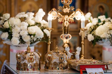 Altın Ortodoks düğün tacını mücevherler ve dini simgelerle süsleyip beyaz çiçek buketleri sergiliyor ve kutsal bir kilisenin içinde mum yakıyor.