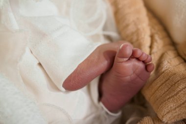 Nazik beyaz kumaş ve rahat bej battaniyeye sarılı yumuşak odaklı bebek ayakları, masumiyeti ve sıcaklığı serin bir ortamda vurguluyor.