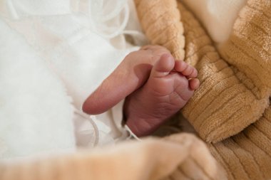 Yeni doğmuş bir bebeğin narin ayaklarının yumuşak bir yakın çekimi. Beyaz dantelli, bej bir battaniyeye sarılı. Yumuşak dokular sergileniyor.