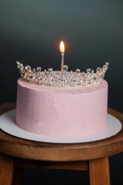 Güzel dekore edilmiş bir pembe doğum günü pastası mücevherli bir taç ve parlak bir mumla süslenmiş, koyu bir zemin üzerine kurulmuş, kutlamalar, partiler veya şenlik için ideal.