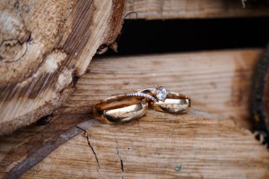 Zarif altın alyansların yakın çekimi ve yıpranmış ahşap üzerine takılmış elmas bir nişan yüzüğü evlilik ya da evlenme teklifi teması için ideal kırsal cazibe ve romantik sembolizmi yakalıyor.