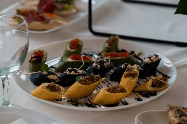 Havyar, ot ve sos yağmuruyla süslenmiş renkli suşi dürümleri rafine bir yemek ortamında beyaz bir tabakta sergileniyor.