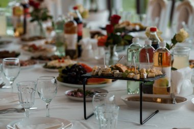 Çok güzel düzenlenmiş bir açık büfe masasında bir gurme peynir tabağı, taze üzümler, karpuz dilimleri, çiçek süslemeleri ve içecek şişeleri, lüks düğünler, resepsiyonlar veya kutlama toplantıları için idealdir.