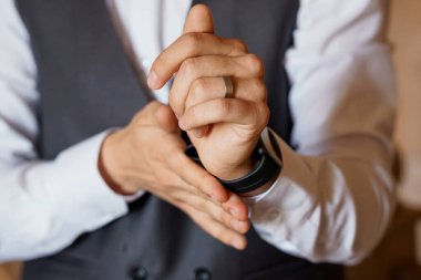 Gıcır gıcır beyaz gömlek ve siyah yelek giyen bir adam düğün hazırlıkları sırasında şık resmi kıyafetler ve zarif aksesuarlar sergileyerek alyansını ve zekasını ayarlar.