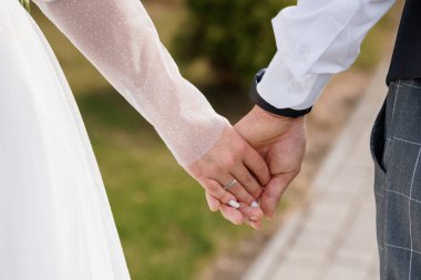 Gelin ve damadın el ele tutuşması, alyansların ve zarif giysilerin sergilenmesi, açık havada aşkın ve bağlılığın sembolü olan bir an.