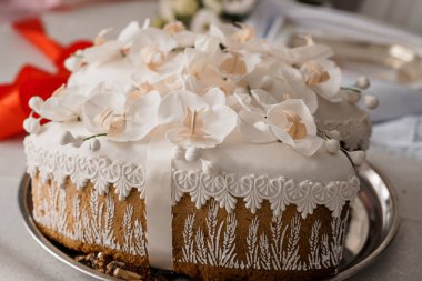 Beyaz orkideler, karmaşık dantel borular ve buğday motifleriyle süslenmiş güzel dekore edilmiş bir düğün pastası, yumuşak ışıklandırma ve romantik ortam ile gümüş bir tepside sunuluyor.