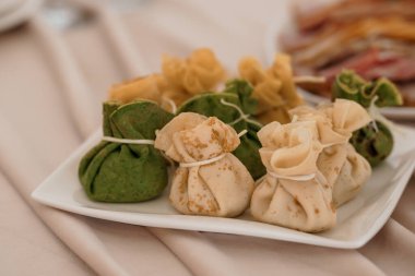 İple bağlanmış yeşil ve bej renkli hamur köftelerinin yakın plan çekimi, beyaz bir tabakta sergileniyor, şenlikli yemek ve yemek sunumları için ideal.