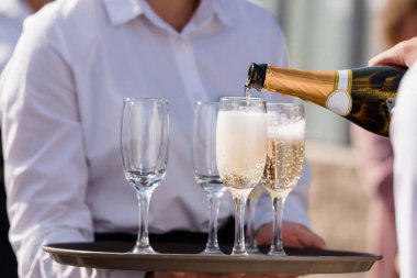 Gıcır gıcır beyaz gömlekli bir garson sofistike bir kutlama sırasında ya da resmi bir toplantı sırasında şık flütlere şampanya döker.