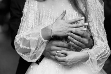 Gelin ve damadın romantik siyah-beyaz yakın çekimi. Elleri görünür alyanslarla sarılı. Özel günlerinde boncuklu dantel kollar ve duygusal bağlar sergiliyorlar.