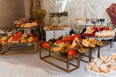 Canlı kırmızı karpuz, altın ananas ve mor üzümlerle dolu cam tezgahlarda sofistike bir etkinlik alanında beyaz örtülere karşı hazırlanmış müsrif bir tatlı ve meyve büfesi.